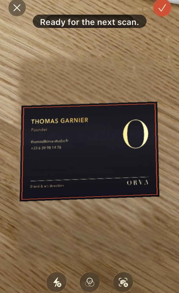 Scanning a black business card with gold lettering, lying on a wooden table.