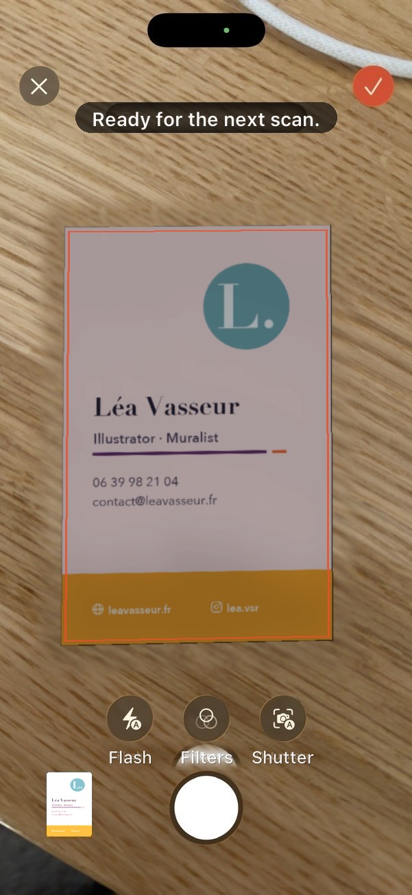 An iPhone photographs a business card lying on a wooden table; Comlynk detects the card and shows “Ready for the next scan”.